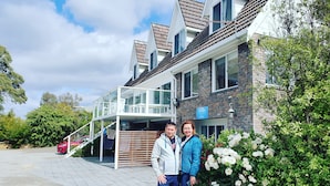 Et toetagers hus med balkon, indkørsel og have med hvide blomster.
