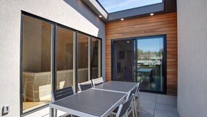 A modern patio with a dining table and chairs, large sliding glass doors, and a view of the surrounding area.