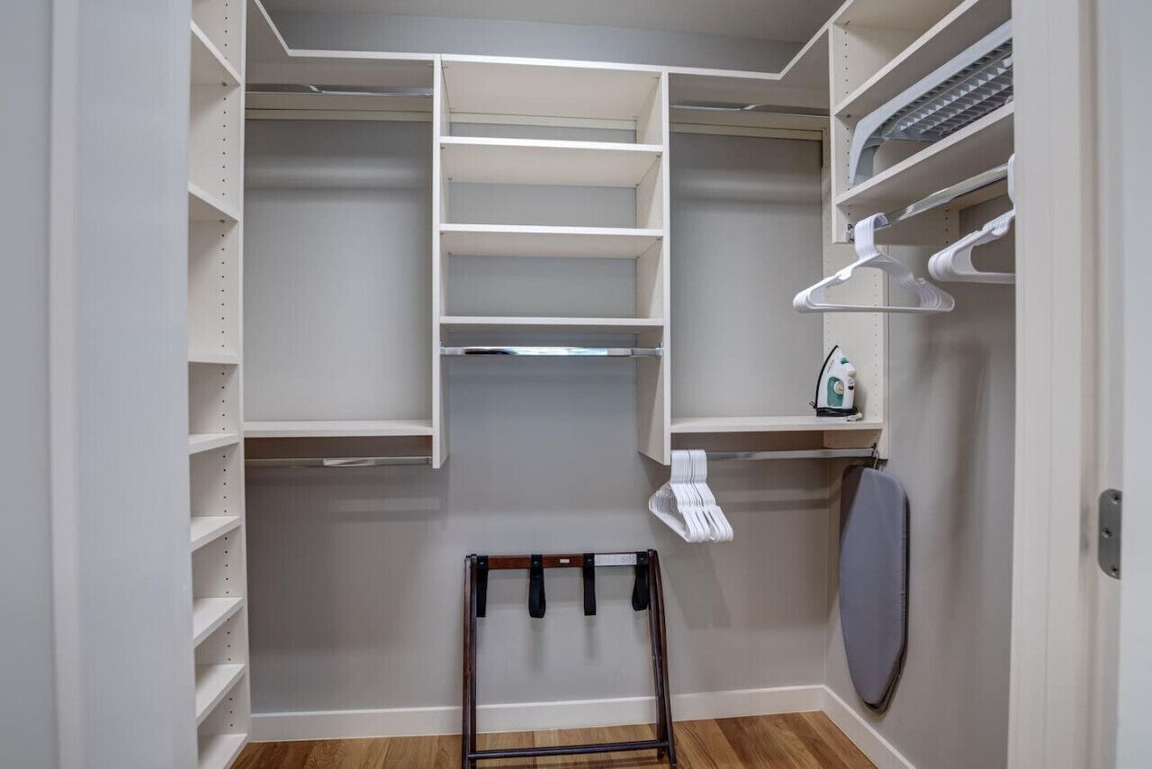 A walk-in closet with multiple shelves and hanging space, a small ironing board, and a towel rack.