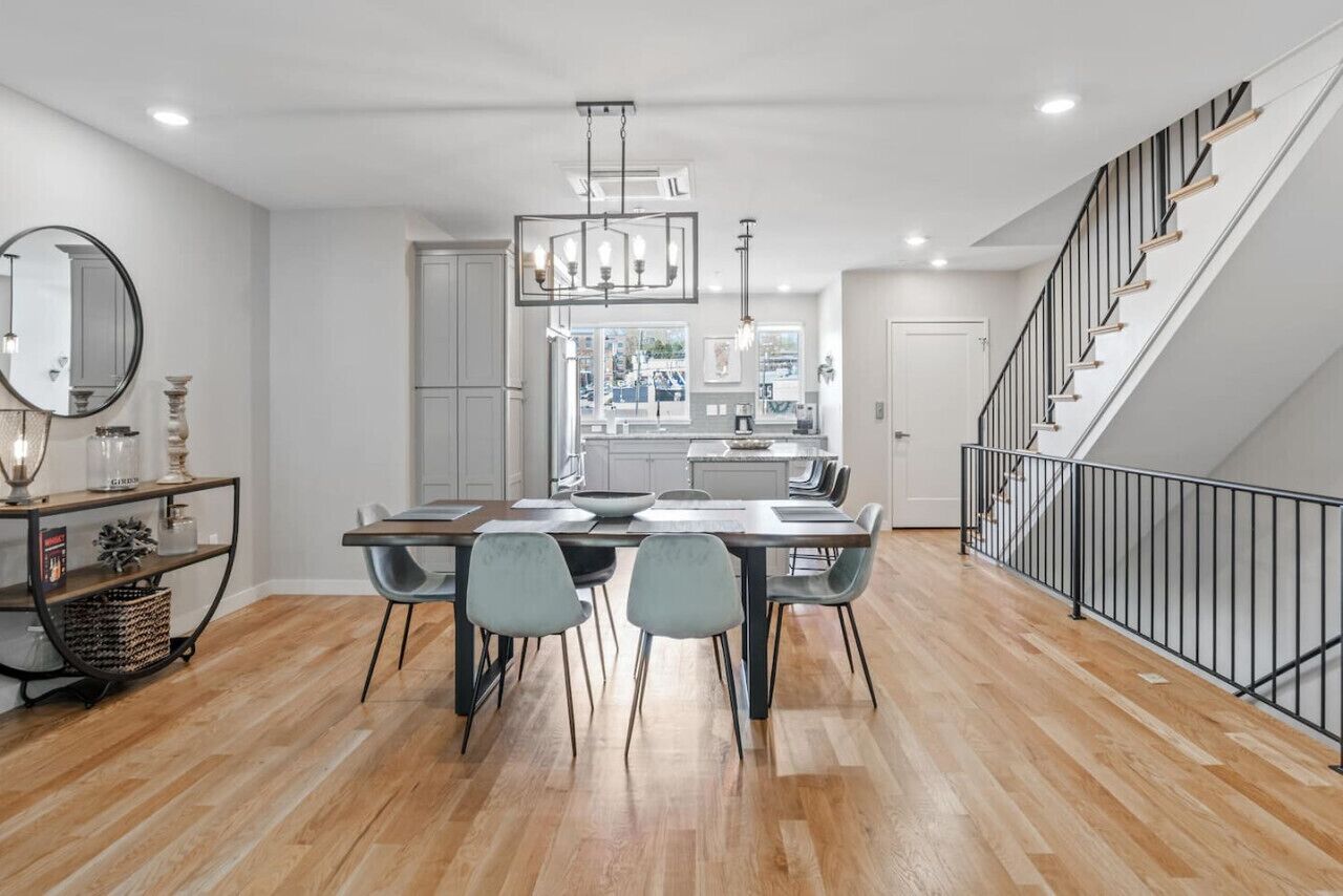 A modern kitchen with a central island, a dining area with a table and chairs, and a staircase with a railing.