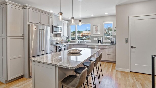 A modern kitchen with white cabinetry, stainless steel appliances, a granite countertop, and pendant lighting.