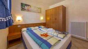 A bedroom with a bed, wooden wardrobe, nightstand, wall-mounted light, and a radiator. - Berna, Livigno, Italy (Livigno)
