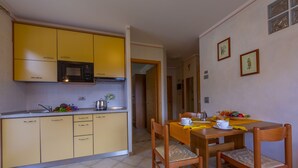 A compact kitchen with yellow cabinets, a microwave, and a dining area with wooden chairs and a table set for two. - Berna, Livigno, Italy (Livigno)