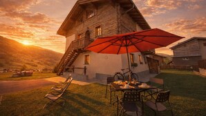 A rustic wooden house with a balcony, a dining table with chairs, and a red umbrella. - Berna, Livigno, Italy (Livigno)