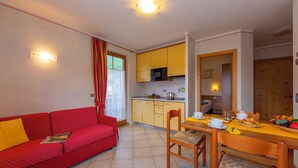 A compact living space with a red sofa, wooden dining table, yellow cabinets, and a kitchen area. - Berna, Livigno, Italy (Livigno)