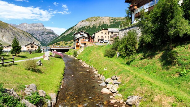 A mountain village with a stream running through it, houses with balconies, and a bridge in the background. - Berna, Livigno, Italy (Livigno)