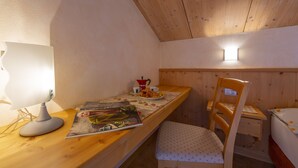 Une pièce confortable avec un bureau en bois, une chaise, un lit et une petite table sur laquelle se trouvent une lampe et un magazine.
