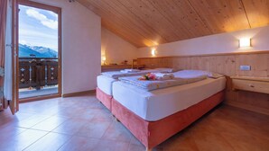 Une chambre avec un plafond en bois, un lit avec des oreillers et une couverture, une table de chevet et une vue sur les montagnes par la porte.