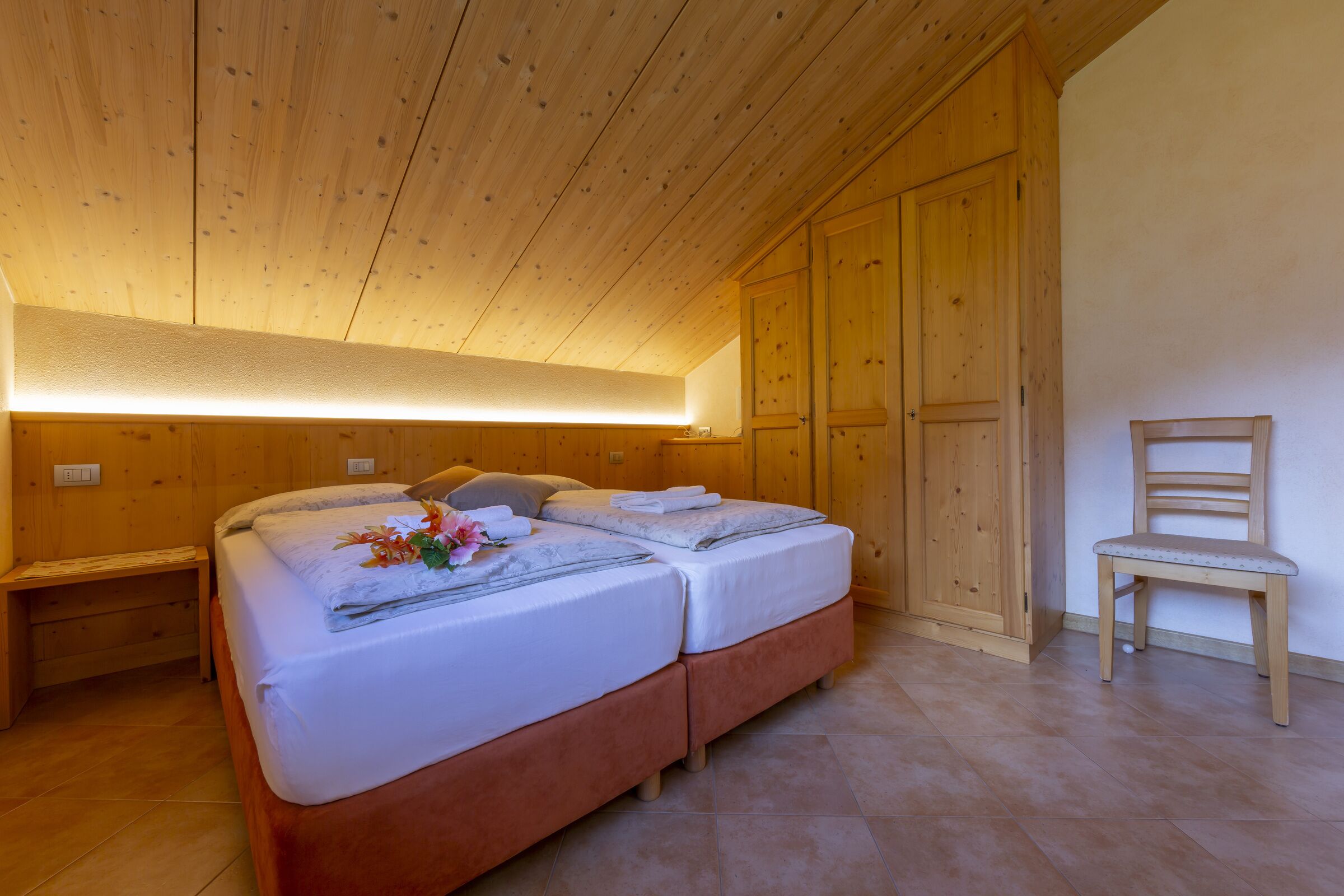 A bedroom with a wooden ceiling, two beds, a nightstand, and a chair.
