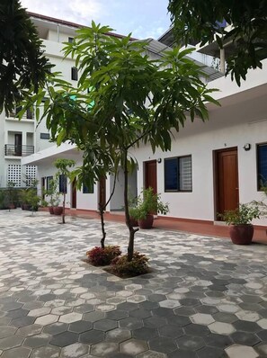A courtyard with hexagonal tiled flooring, potted plants, and a white building with multiple doors and windows. - MN Apartment (Siem Reap)