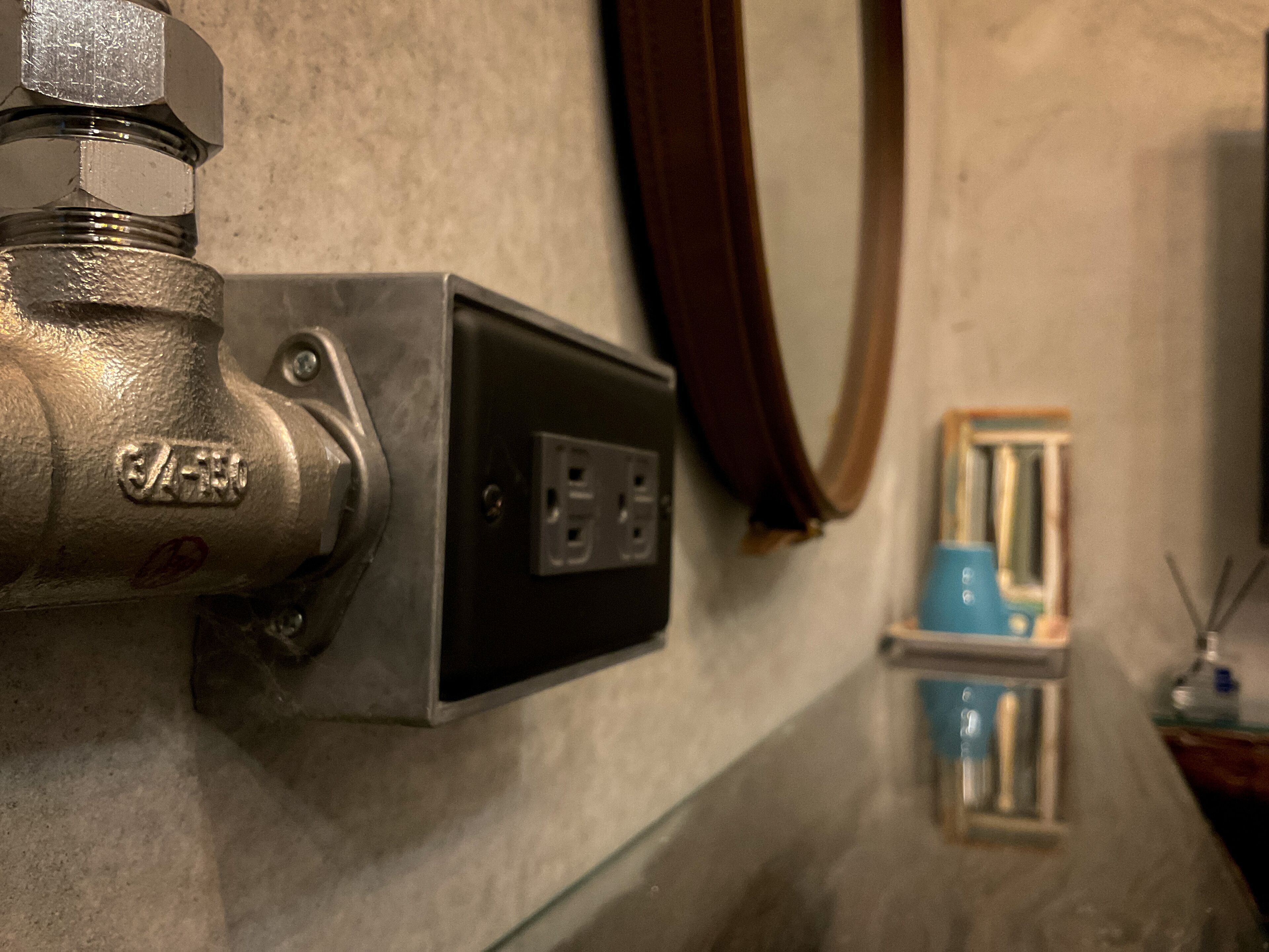 A bathroom with a visible water spigot, electrical outlet, and a mirror.