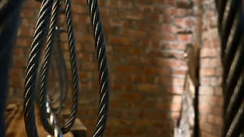 A close-up of a metal structure with twisted ropes, a brick wall, and a clock in the background.