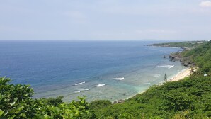 A coastal landscape with a beach, clear blue sea, and lush greenery. - Little Ryukyu Hermit Crab Homestay (Liuqiu)