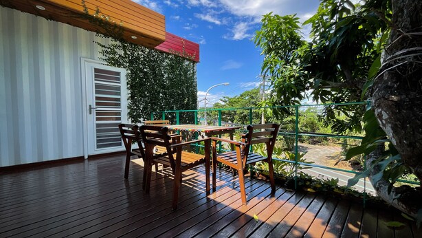 A wooden deck with a table and chairs, a white door, and a green wall with climbing plants. - Little Ryukyu Hermit Crab Homestay (Liuqiu)