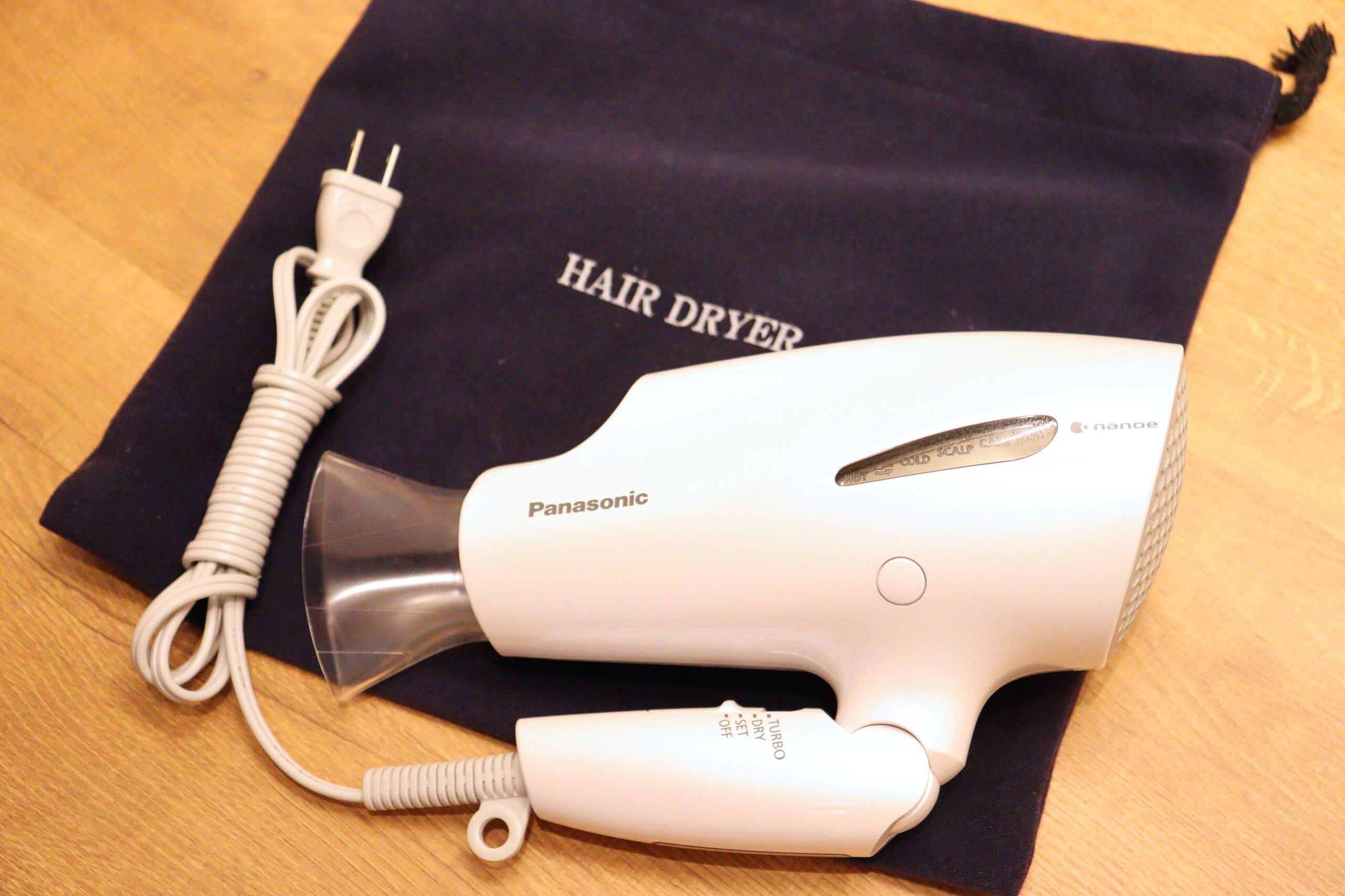 En Panasonic hårtørrer med ledning, placeret på et mørkt klæde med teksten 'HAIR DRYER'.