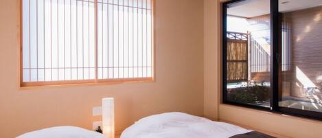 Habitación con dos camas, una ventana con persianas verticales y vista a una estructura de madera en el exterior.
