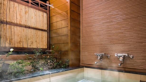 Ein traditionelles japanisches Badezimmer mit einem Holzboden, einer Steinschüssel und einem Holzeimer.