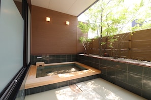 Un baño moderno con bañera hidromasaje integrada, paredes de baldosas oscuras y un banco de madera.