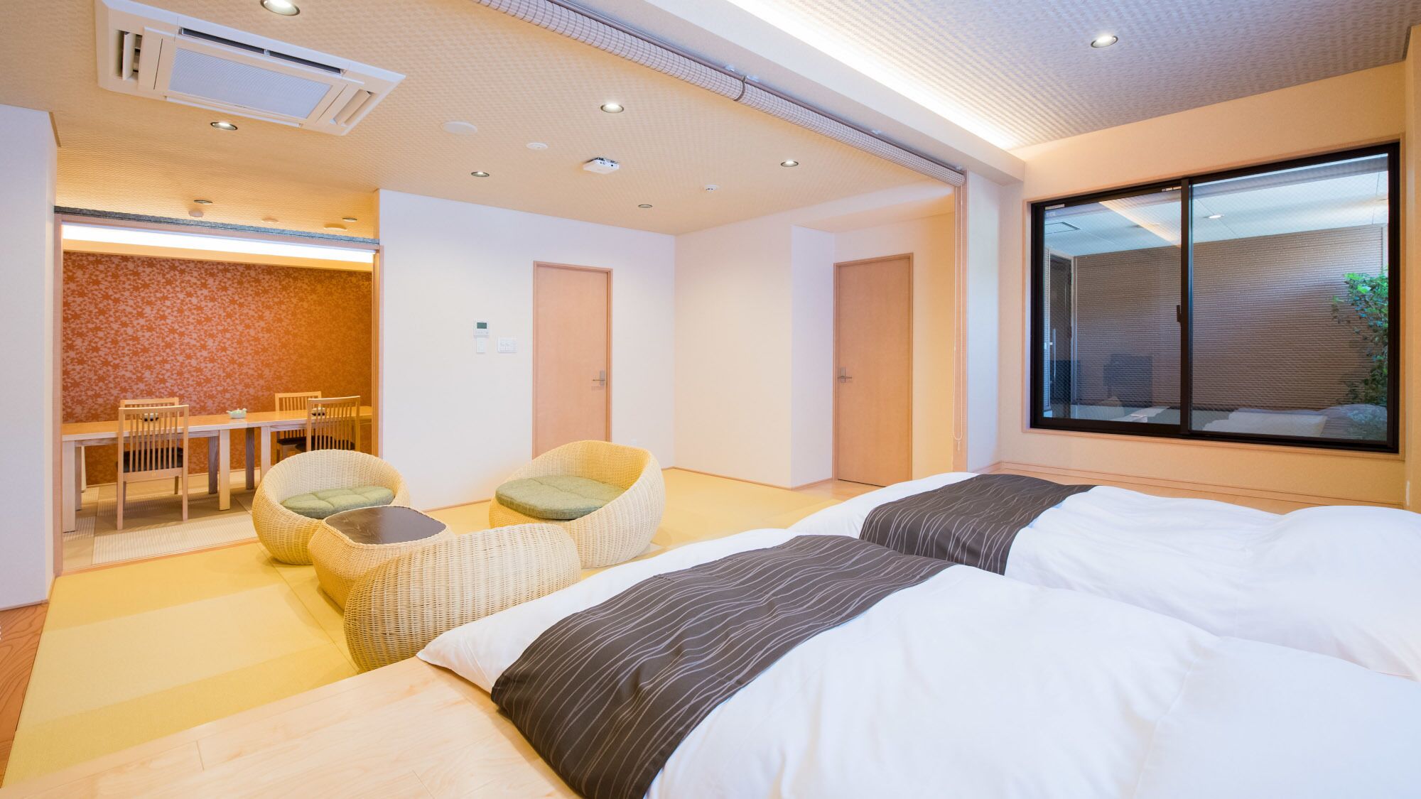 A hotel room with two beds, a dining area, and a view of the outside.