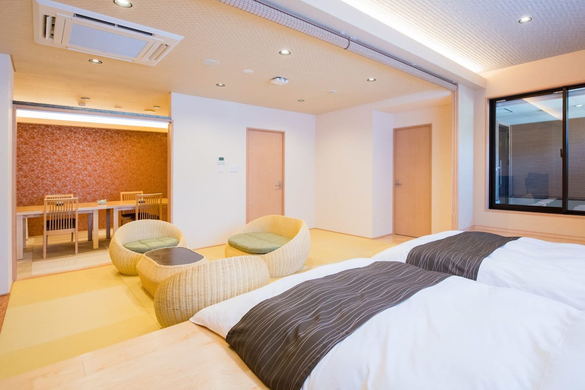 A hotel room with two beds, a dining area, and a view of the outside.