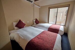 A hotel room with two beds, each with a red and white bedspread, a window with blinds, and an air conditioning unit on the wall. - Tsumugi Horikawakichimonji (Kyoto)