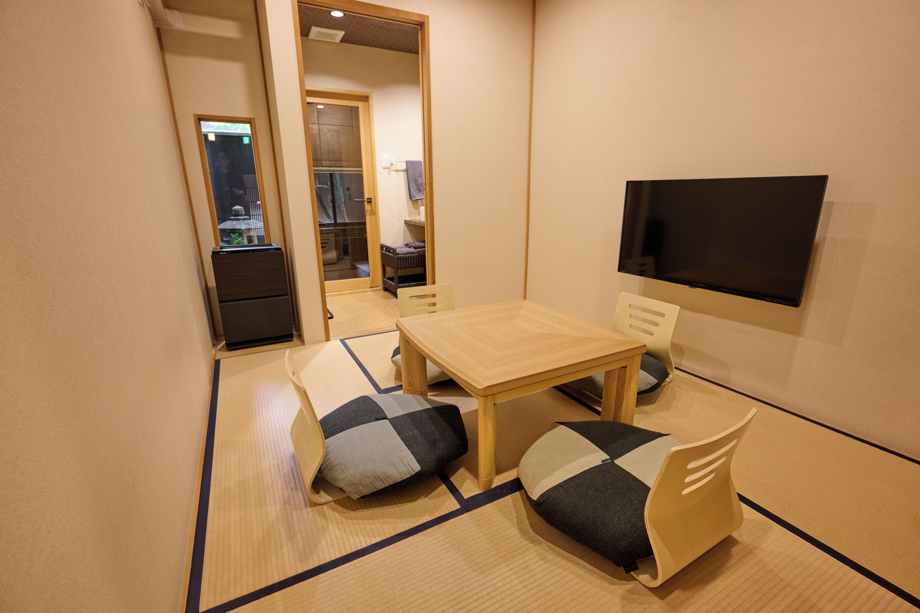 Een kleine kamer met tatami vloer, een lage houten tafel, twee stoelen, een televisie en een spiegel.