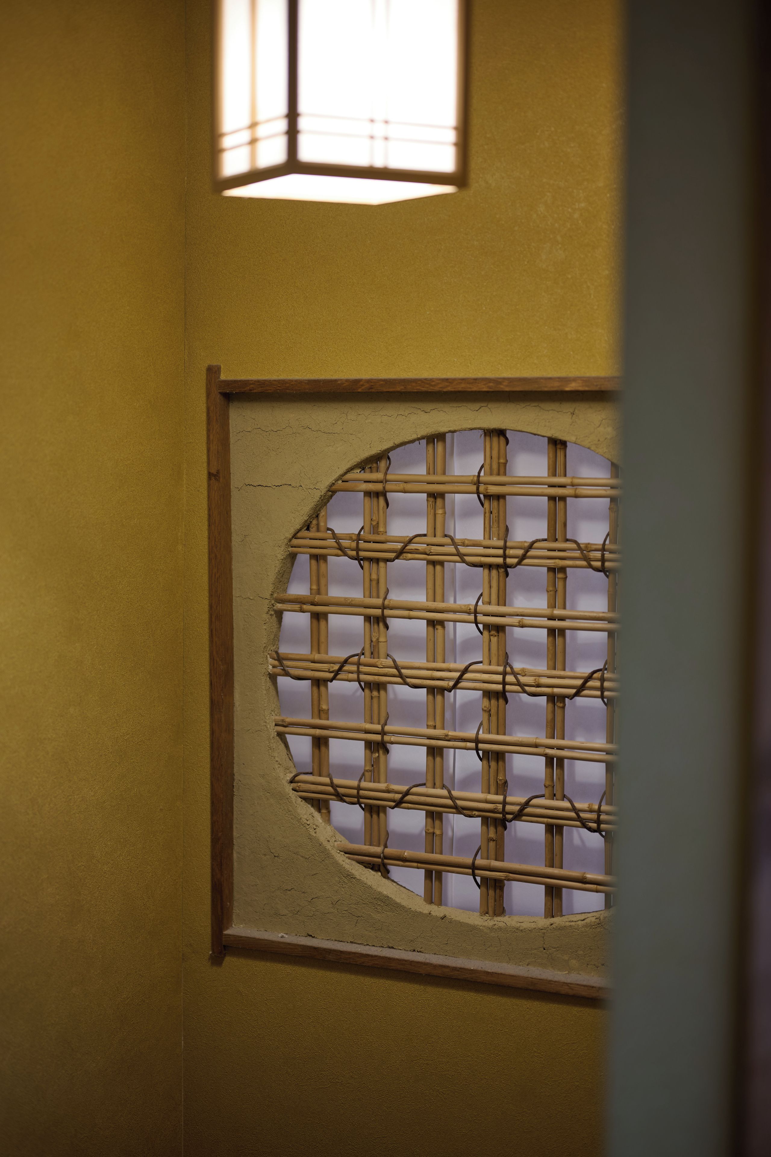 Eine Wand mit einem runden Fenster, das ein Bambusgitter-Muster zeigt.
