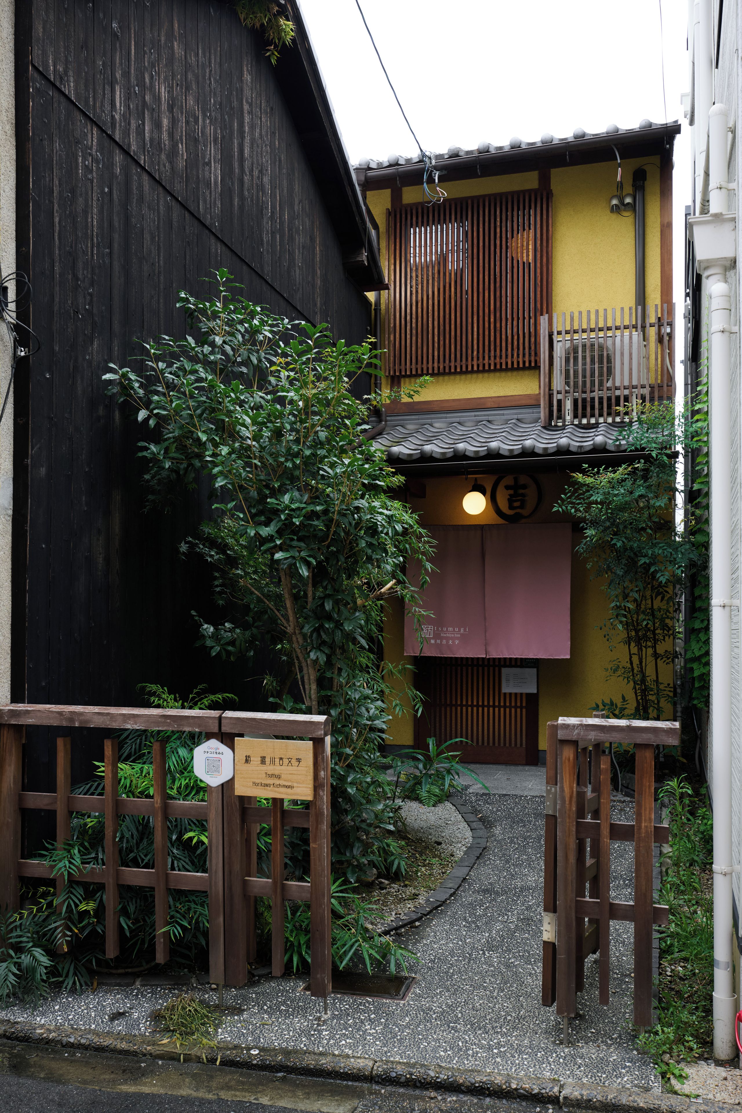 A traditional Japanese building with a wooden gate, a small garden, and a sign indicating the name of the establishment.