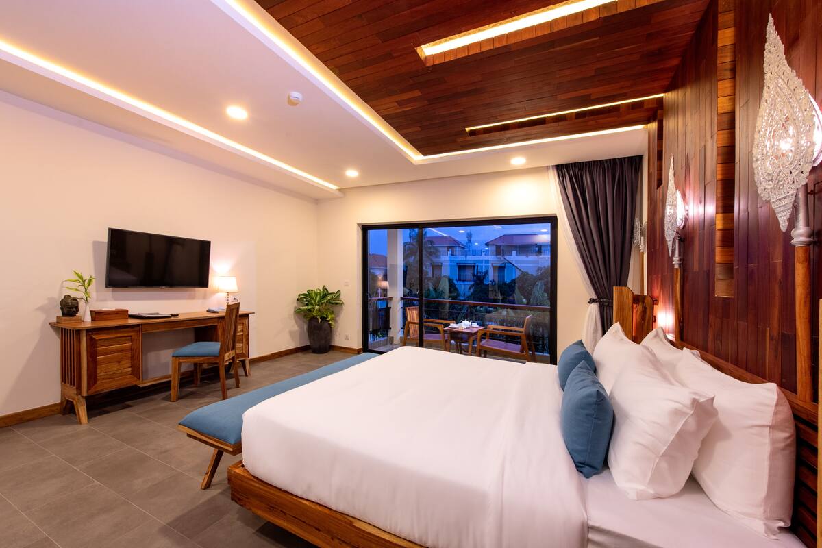 A modern hotel room with a large bed, a desk with a TV, and a balcony with a view.