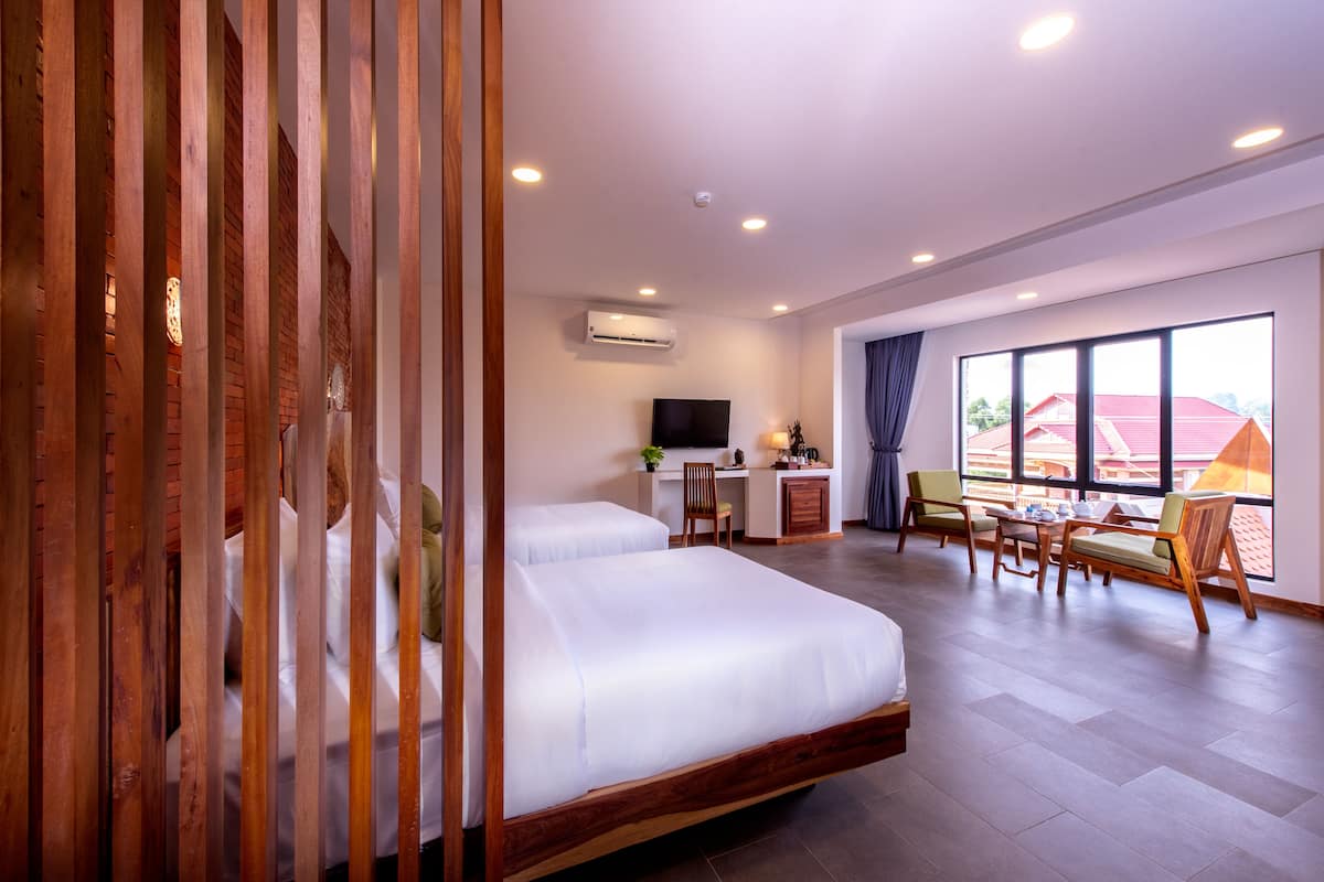 A hotel room with two beds, a desk, a chair, a TV, and a large window.