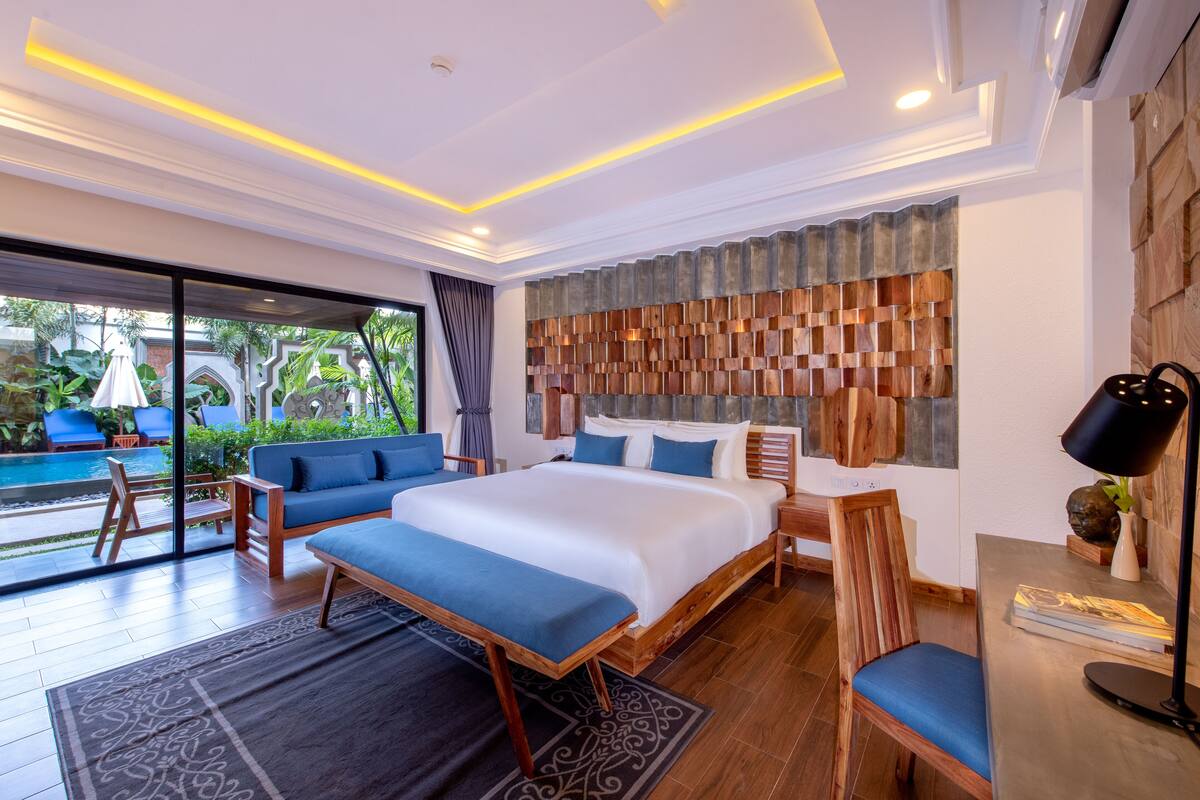 A modern hotel room with a large bed, a sofa, a desk, and a view of a swimming pool.