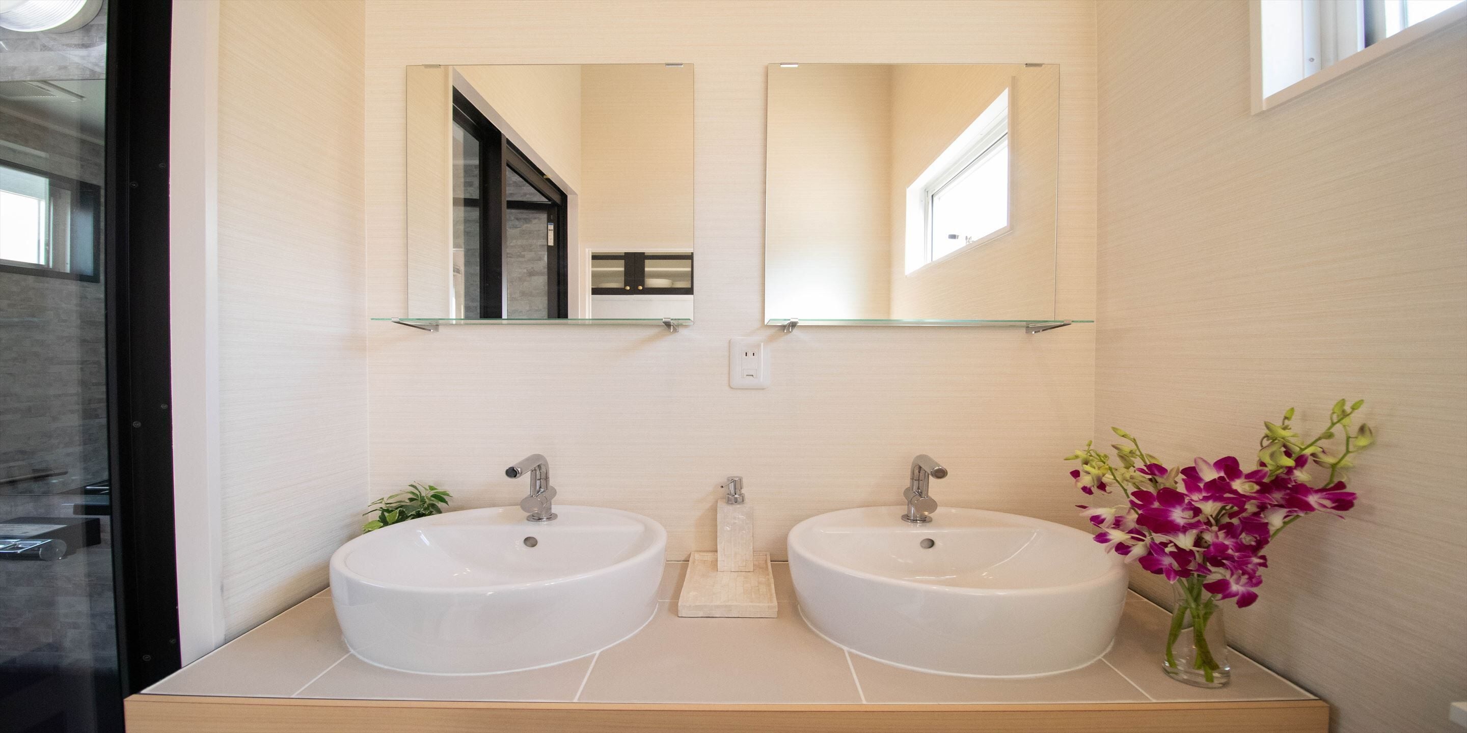 A modern bathroom with two sinks, a mirror above each, and a vase of flowers on the right.