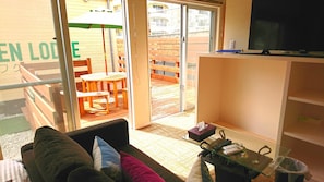 A living room with a sofa, a glass coffee table, and a TV on a stand. - Okinawa Green Lodge (Chatan)