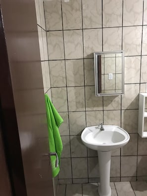 Un baño con un lavamanos pedestal blanco, un espejo y una toalla verde colgada del pomo de la puerta.