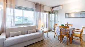 Una sala de estar moderna con sofá, mesa de comedor, sillas y un amplio ventanal con vistas a la ciudad.