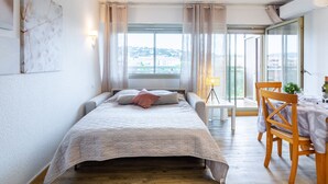 Un dormitorio con cama, escritorio y silla. Se ve una ventana con cortinas y vistas a edificios.