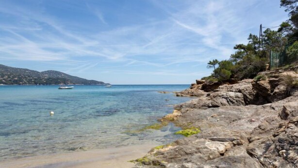 A coastal landscape with clear waters, rocky shore, and a distant boat. - Cap Nègre : Domaine de la Pinède by Interhome (Le Lavandou)