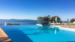 An infinity pool with clear blue water, white lounge chairs, and a view of the sea. - Cap Nègre : Domaine de la Pinède by Interhome (Le Lavandou)