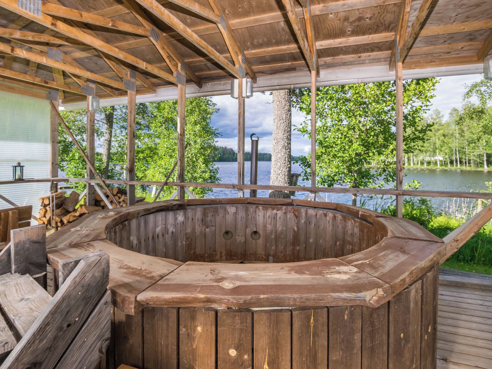 A wooden hot tub on a deck with a view of a lake and trees.