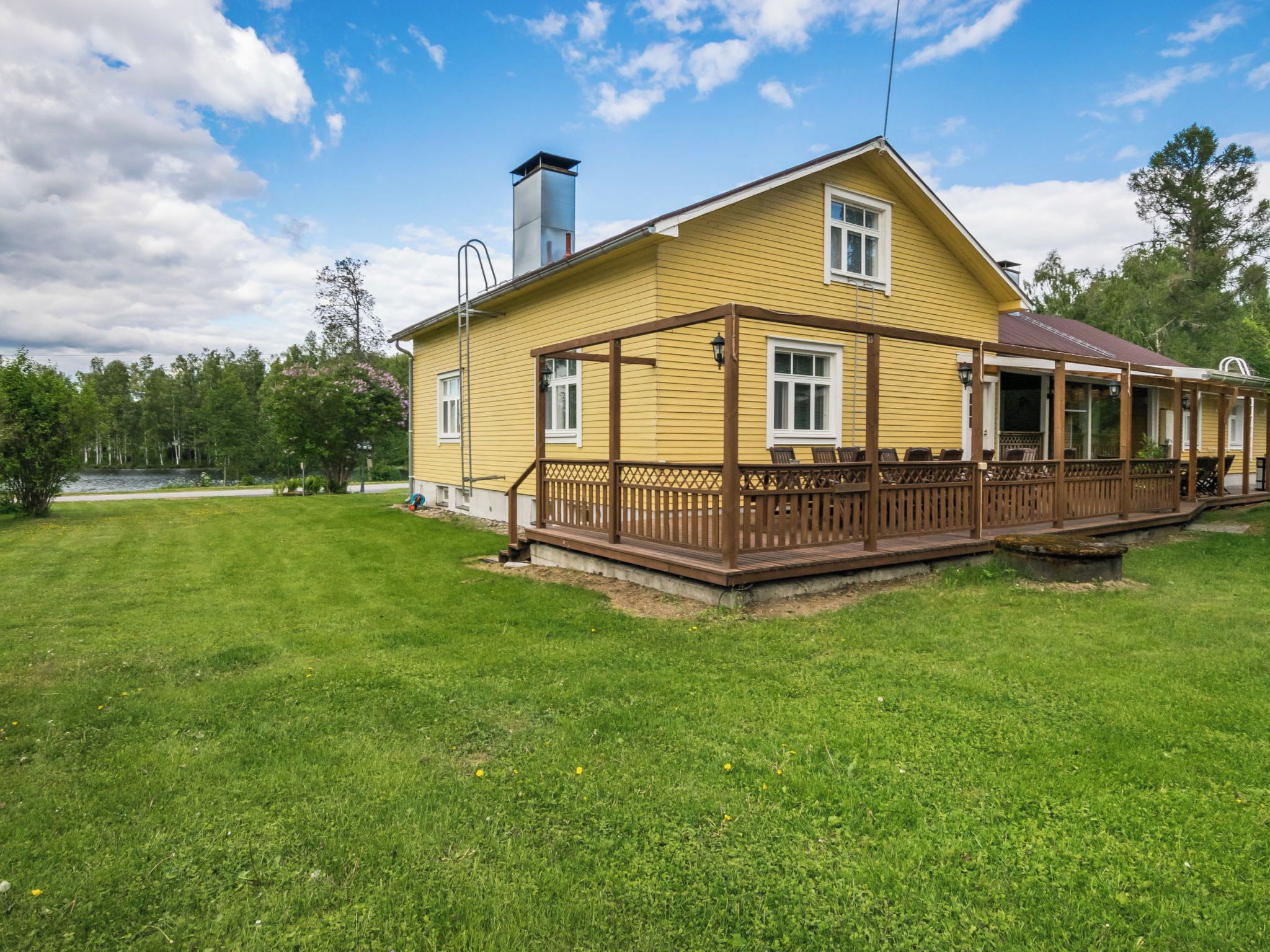 A yellow house with a wooden deck and a chimney.