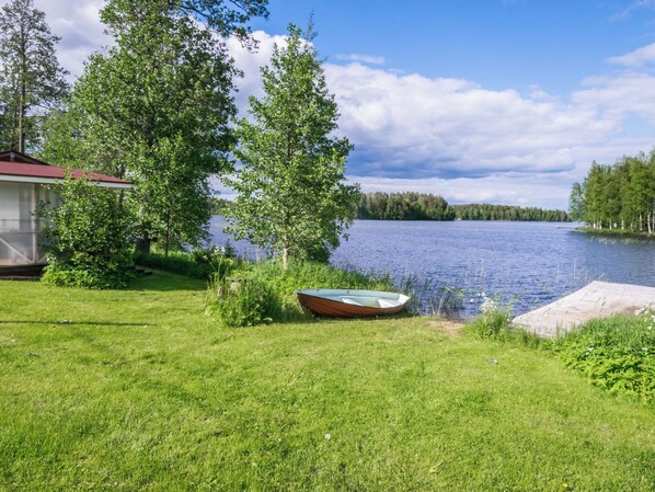 A grassy area with a boat and a dock by a lake, surrounded by trees and a building.