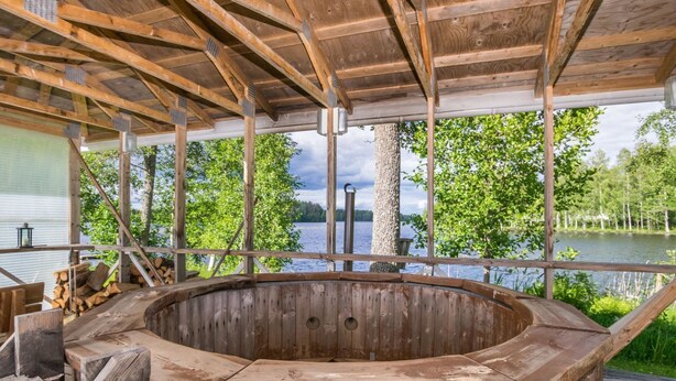 Un bain à remous en bois installé sur une terrasse, avec vue sur un lac et des arbres.