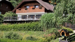 Ein Chalet mit Balkon und einer Holzterrasse, umgeben von üppiger Vegetation.