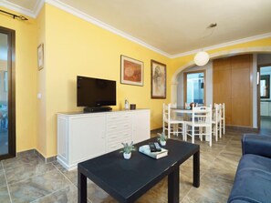 A living room with a TV, white cabinets, a dining table with chairs, and a blue sofa.