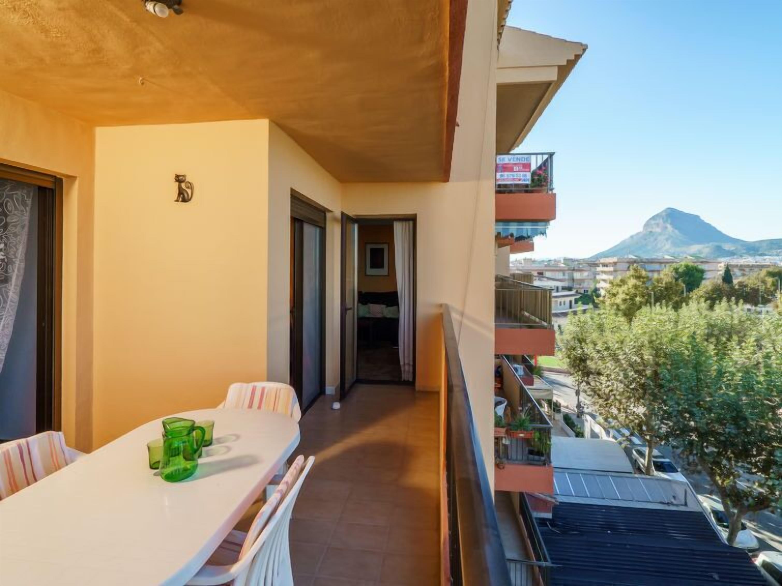 Een balkon met een tafel en stoelen, uitzicht op een berg en een gebouw met een bord.
