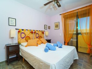 A hotel room with a bed, two bedside tables, a ceiling fan, and a window with orange curtains.