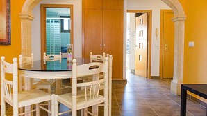 A dining area with a glass table surrounded by white chairs, an archway, and wooden doors. - Galicia Javea by Interhome (Jávea)
