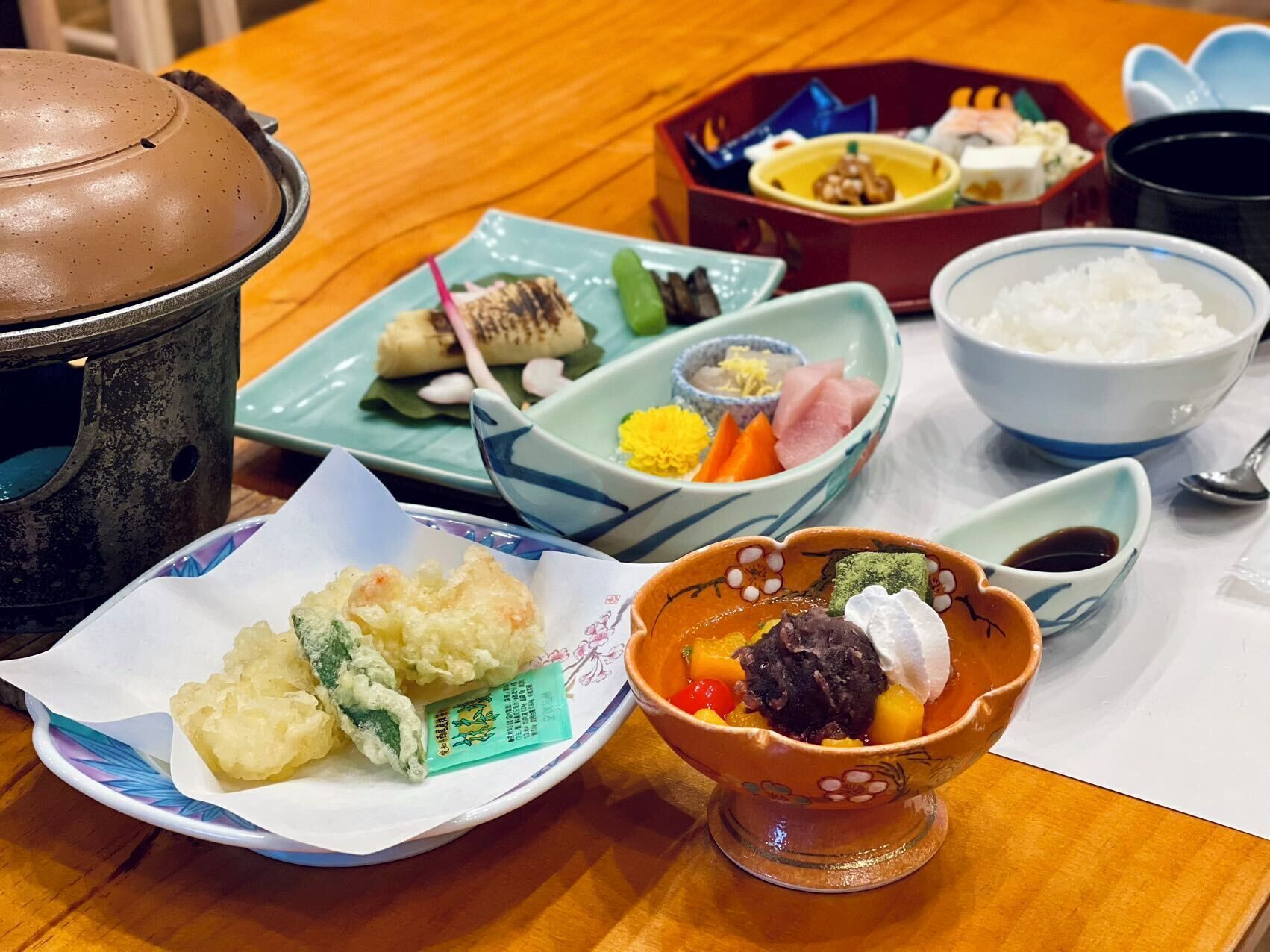 A variety of Japanese dishes on a wooden table, including sushi, rice, and a bowl of soup.