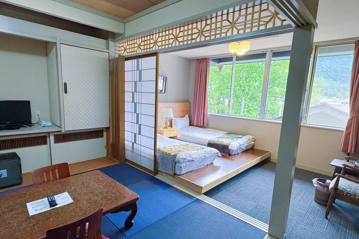 A traditional Japanese-style room with tatami flooring, a low bed with a futon, a desk with a computer, and a sliding shoji screen.