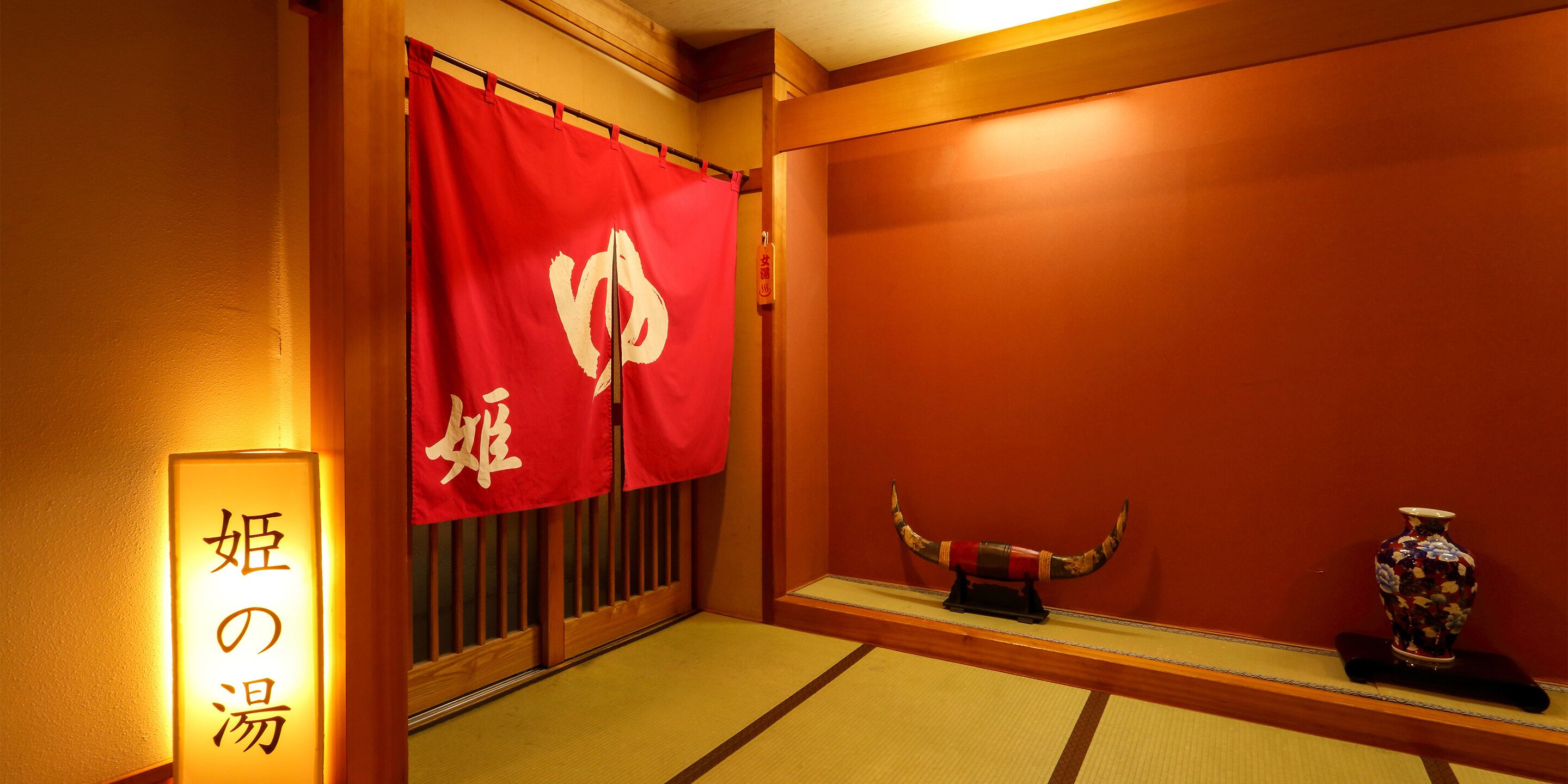 Ein traditioneller japanischer Raum mit Tatami-Bodenbelag, einem roten Shoji-Bildschirm, einer dekorativen Vase und einem Schild mit japanischen Schriftzeichen.